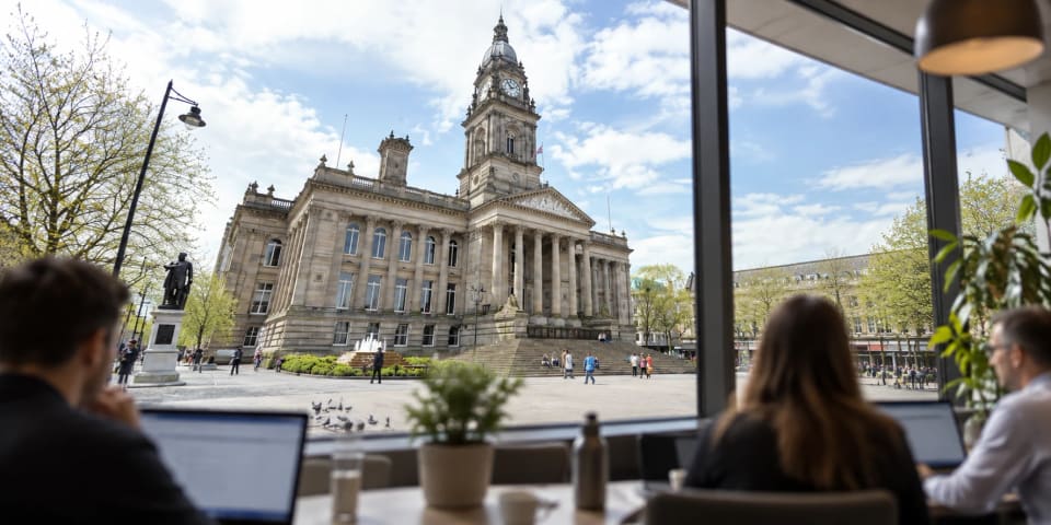 People working on laptops at a table by a large window, looking out across Victoria Square to Bolton Town Hall