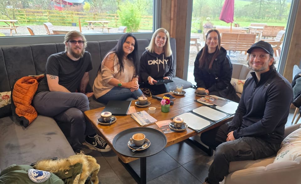 Five members of the CVP Group team smiling around a café table with coffees and notebooks