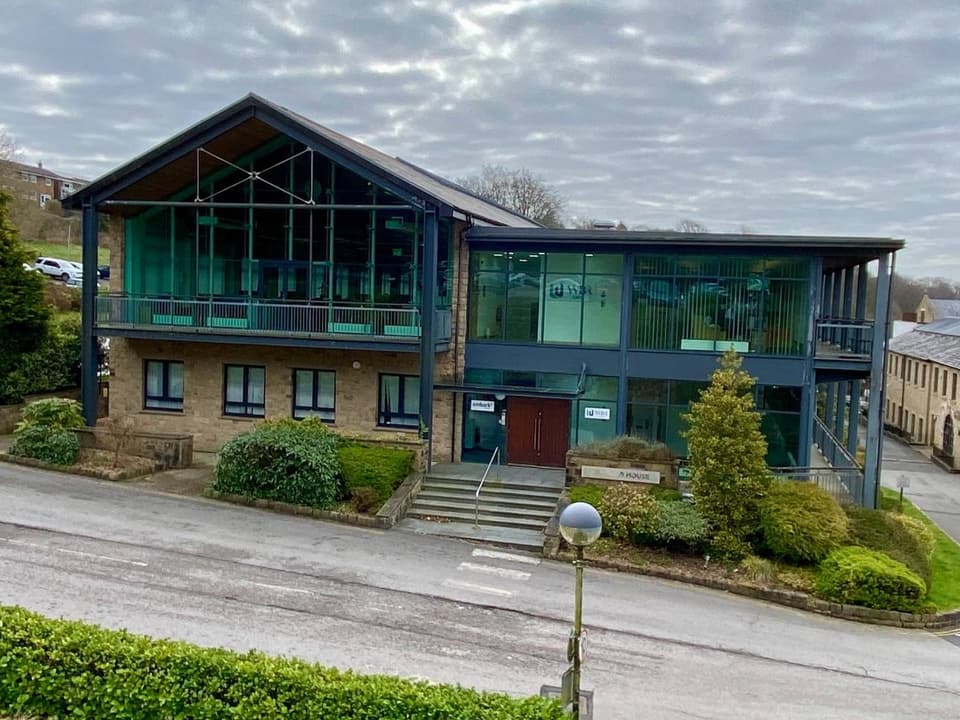 A modern stone and glass office building at Deakins Business Park, Bolton, with landscaped gardens in front